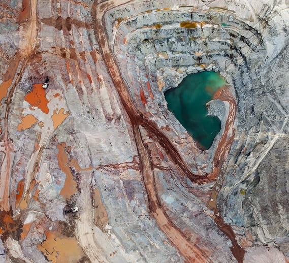  Aerial view of a mining site with distinct layers of red, orange, and gray earth surrounding a vibrant green water pool. The image showcases the vast scale and intricate patterns of the mining landscape, representing the transformative impact of infrastructure projects like the Simandou mining venture in Africa