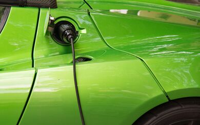 A green electric vehicle connected to a charger