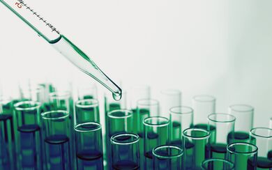 Several rows of test tubes with green liquid and a dropper distributing samples