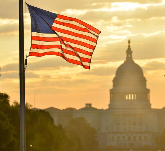 The American Flag flying in the foreground, with the Capitol building faded in the background at sunset