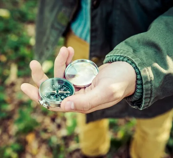 A close-up of a person holding a compass in a forest-like area