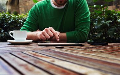 A man using his smartphone and tablet in the outdoor seating area of a peaceful cafe