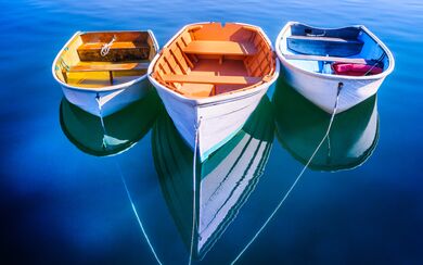 On the surface of a blue lake, three brightly colored little boats are tied together