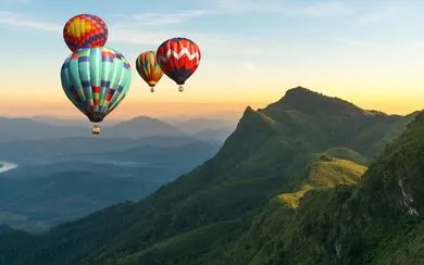 A sunset framed by colorful hot air balloons floating over a green mountain range